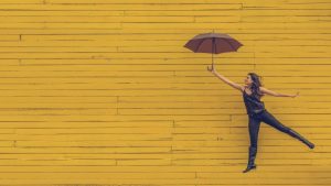Девушка прыгает с зонтом на фоне желтой стены